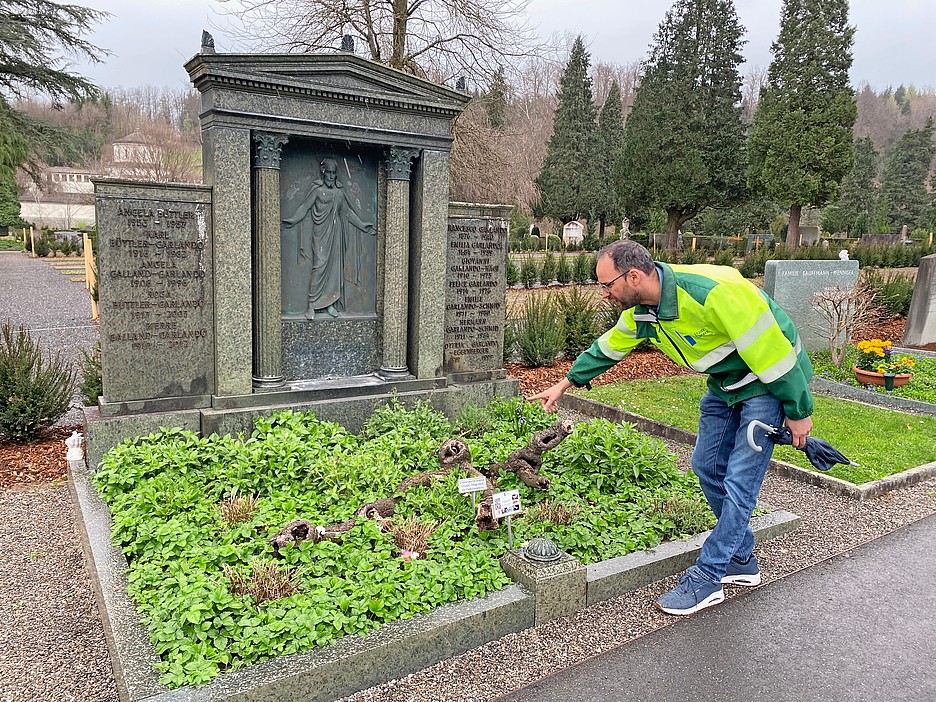 Pascal Vincent zeigt auf ein Grab, das mit einheimischen Pflanzen geschmückt ist.